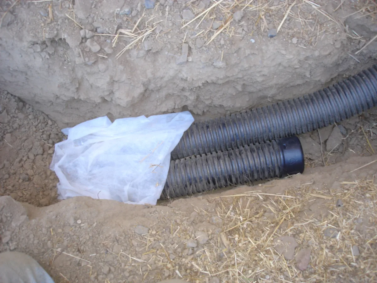 French drain installation showing perforated pipe with white geotextile filter fabric in a residential trench