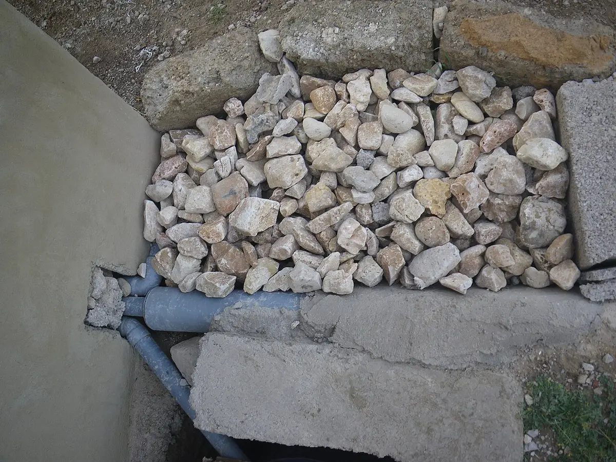 Stone-filled soak pit beside a wall with a gray pipe entering below the stones