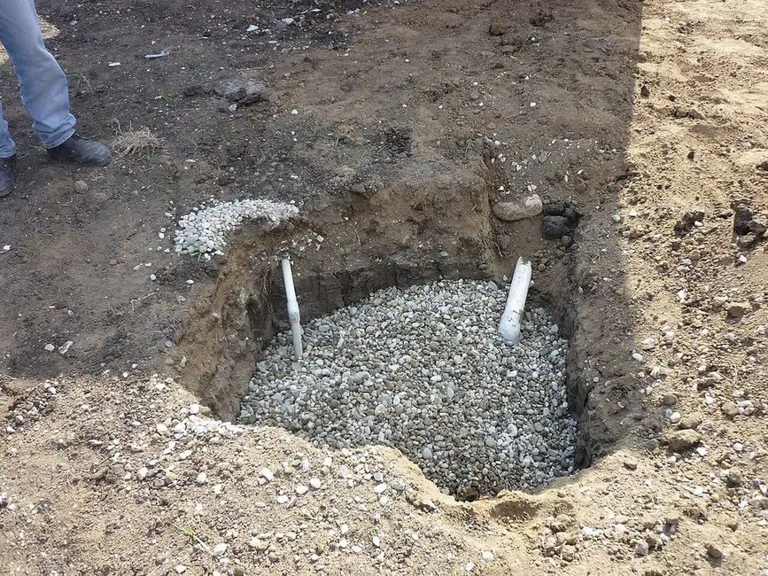 Dry well installation in progress: a gravel-filled pit with two white pipes rising from the stone