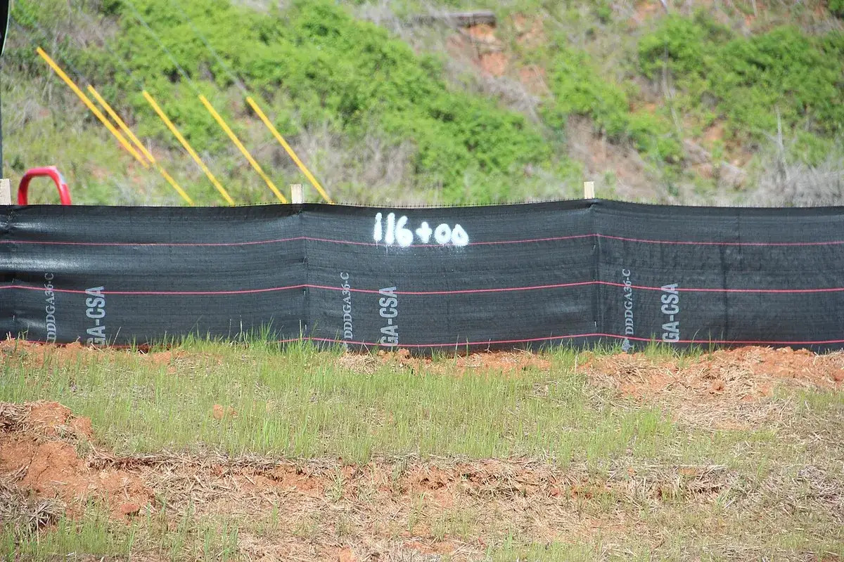 Black silt fence staked along the bottom of a disturbed red clay slope with new grass coming in