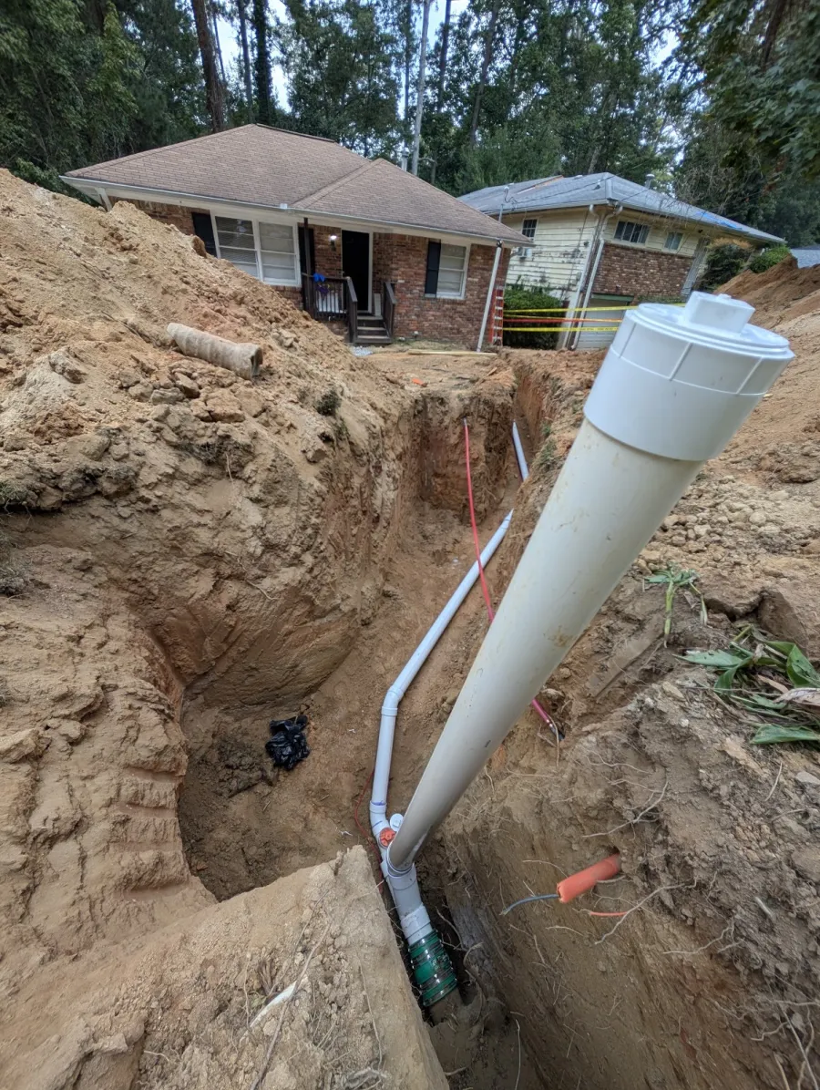A deep trench beside a brick home with a new pipe run and cleanout going in