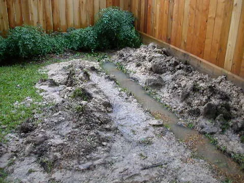 Muddy trench reopened along a wooden fence with water standing in the bottom