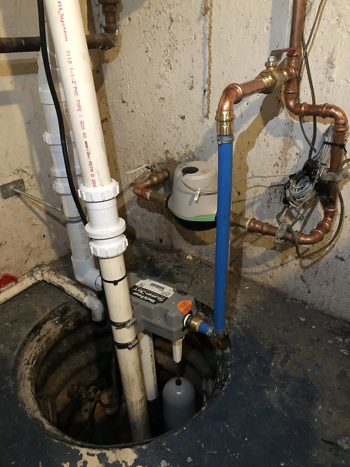 A newly installed basement sump pump in its pit with a white PVC discharge riser running up the wall