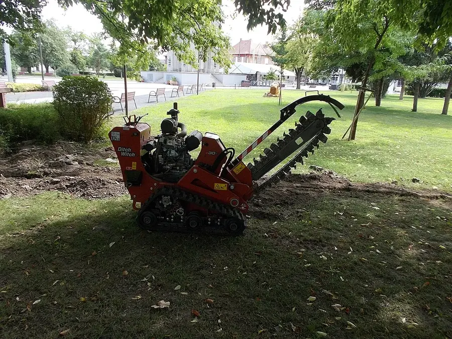 Walk-behind track trencher parked on a lawn beside a freshly cut trench line